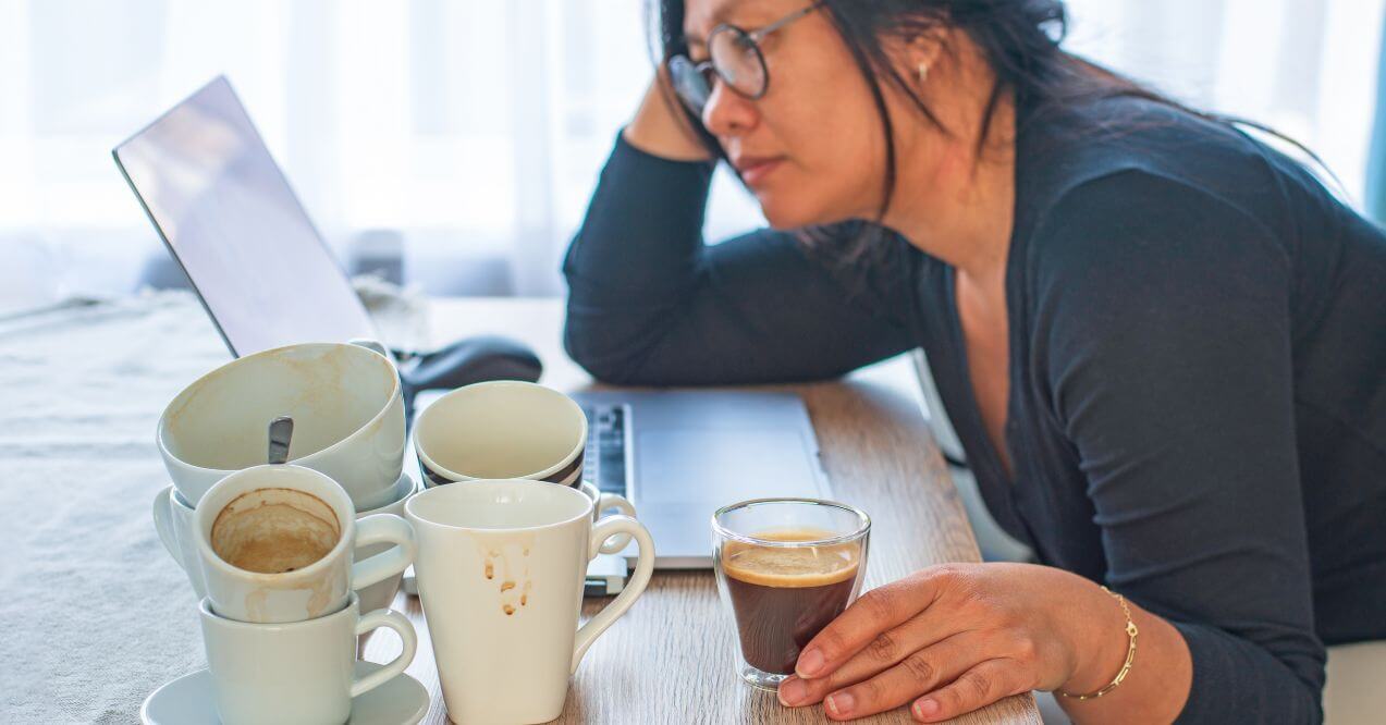 Person surrounded by coffee mugs, appearing tired from an unhealthy lifestyle.