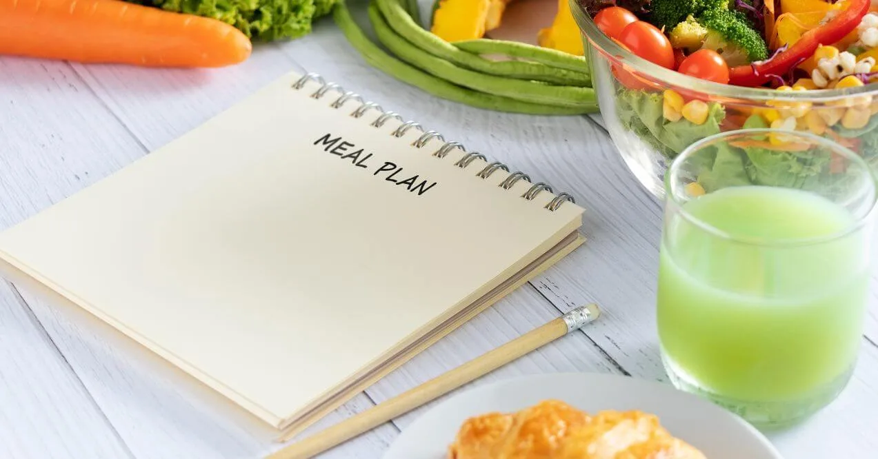 Meal plan notebook with healthy food and a green drink on a wooden table.