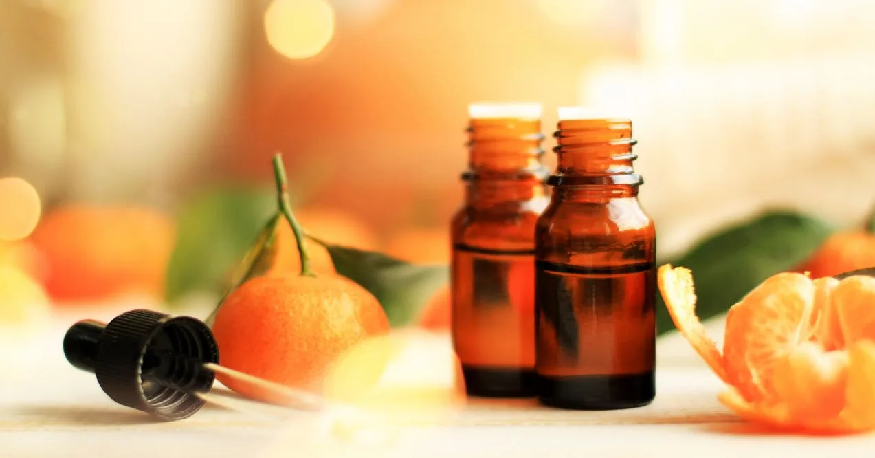 Two amber essential oil bottles with fresh oranges and a warm blurred background.