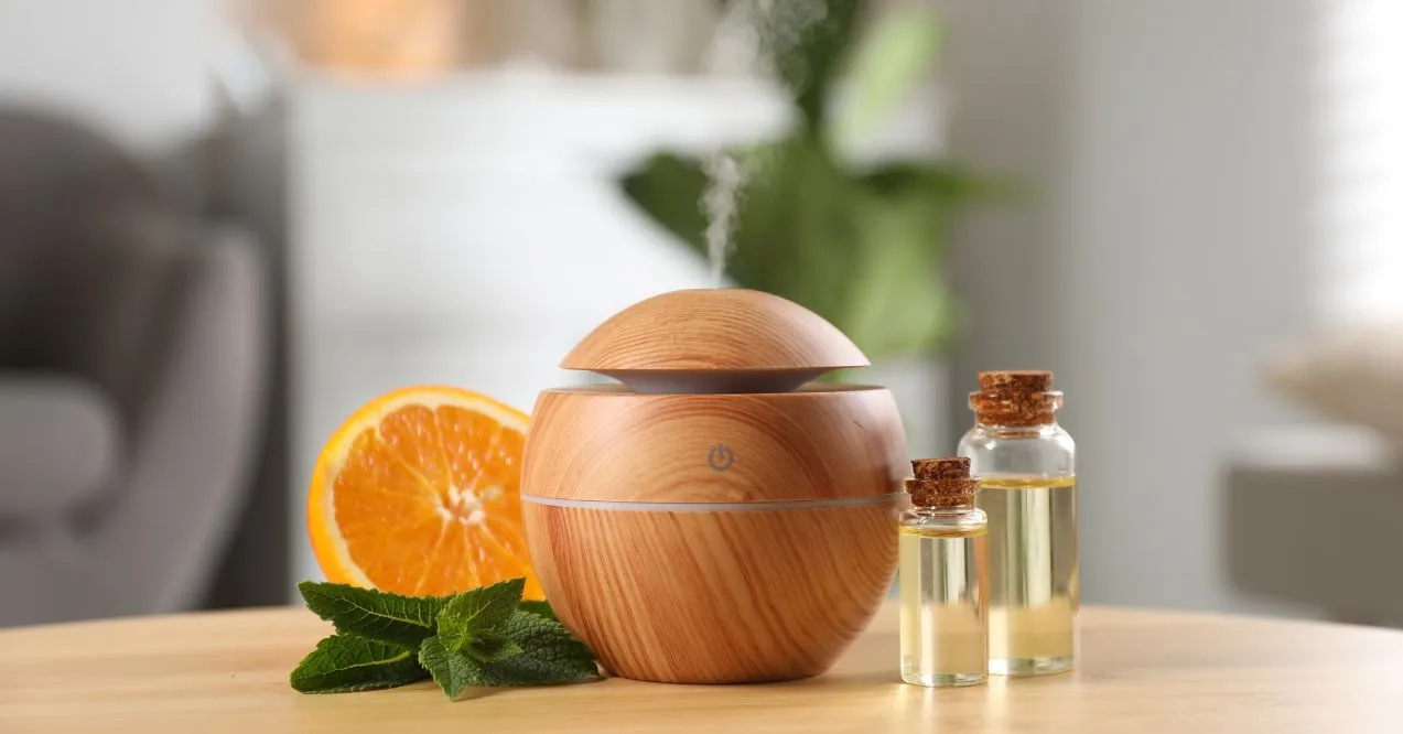 Wooden essential oil diffuser with steam, surrounded by orange slices, mint leaves, and oil bottles.