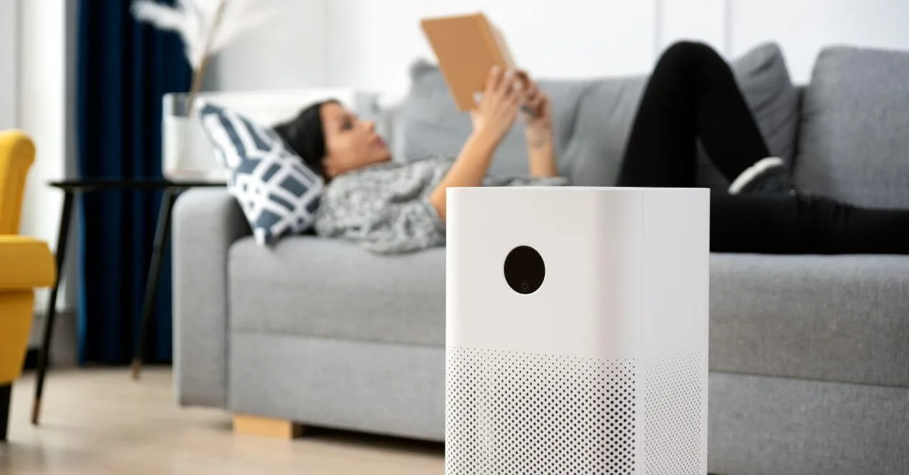 White air purifier in a living room with a woman relaxing on a couch.