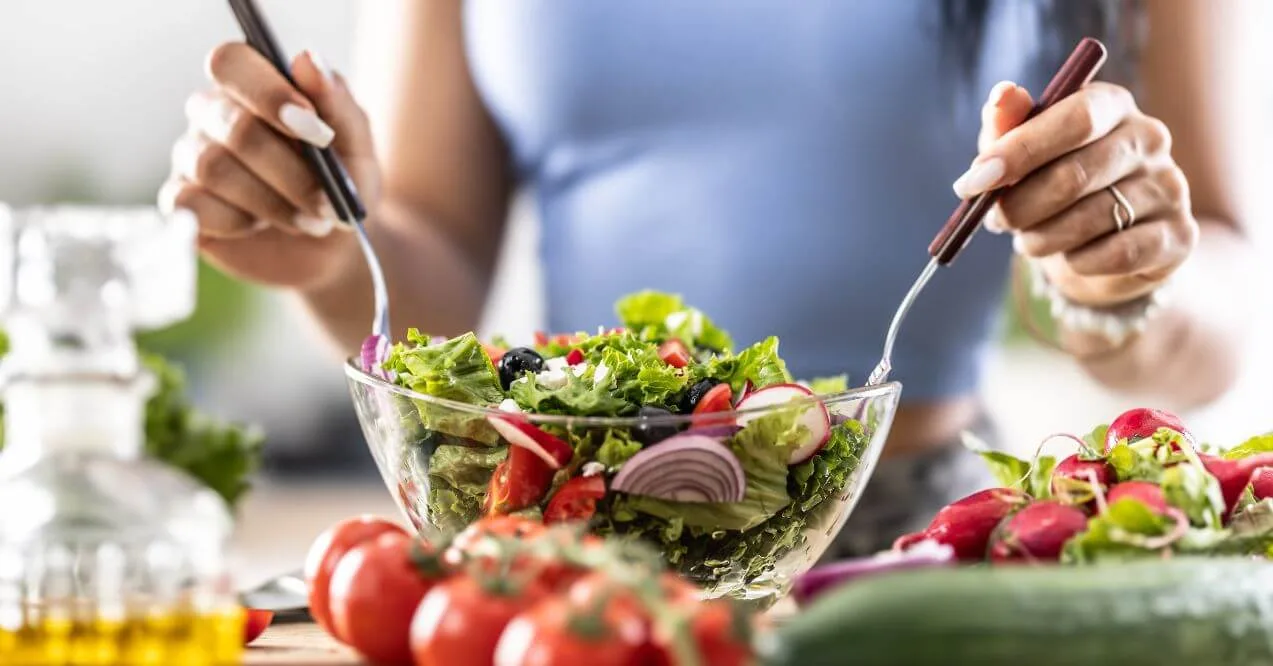 Woman preparing and eating a fresh salad with vegetables.