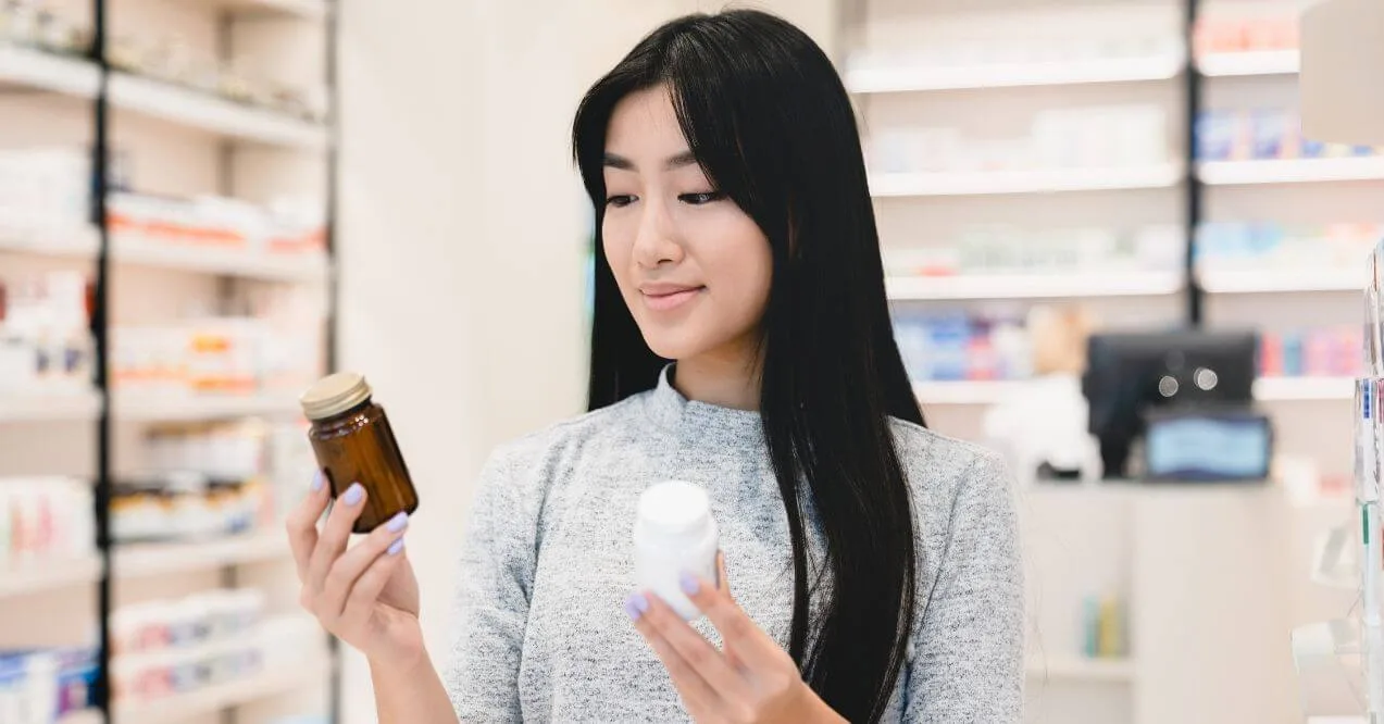 Woman in a pharmacy comparing two supplement bottles.
