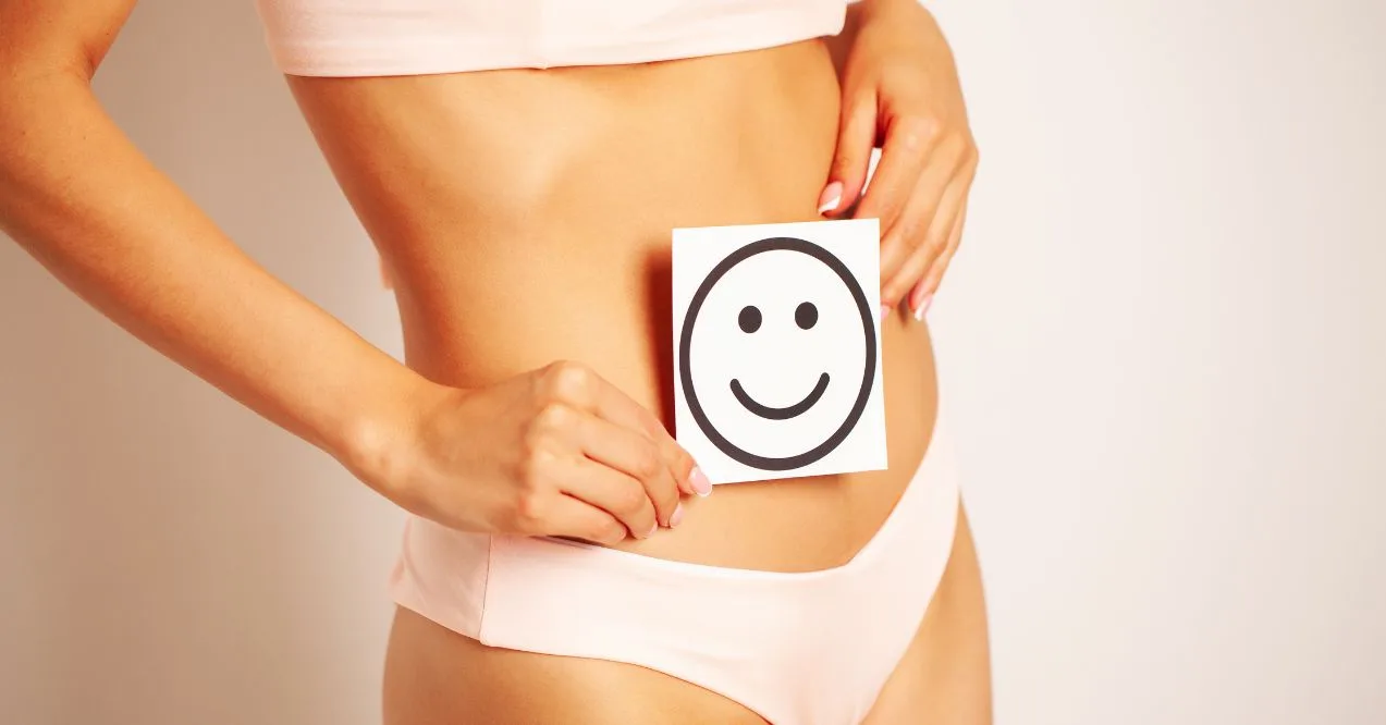 Woman in light-colored underwear holding a smiley face card over her stomach.