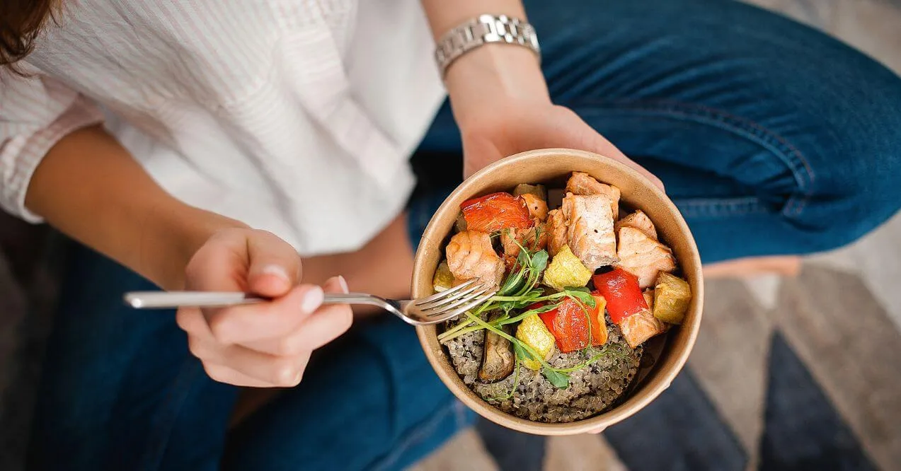 Woman holding a bowl of healthy food with quinoa, salmon, and vegetables.