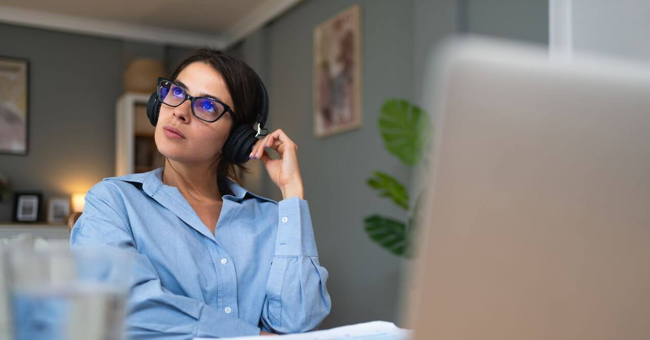 Woman wearing glasses and headphones, sitting by the desk, thinking how to improve attention span