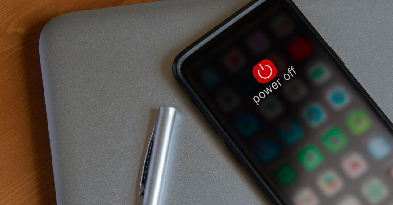 Smartphone screen showing a "Power Off" icon resting on a laptop next to a pen.