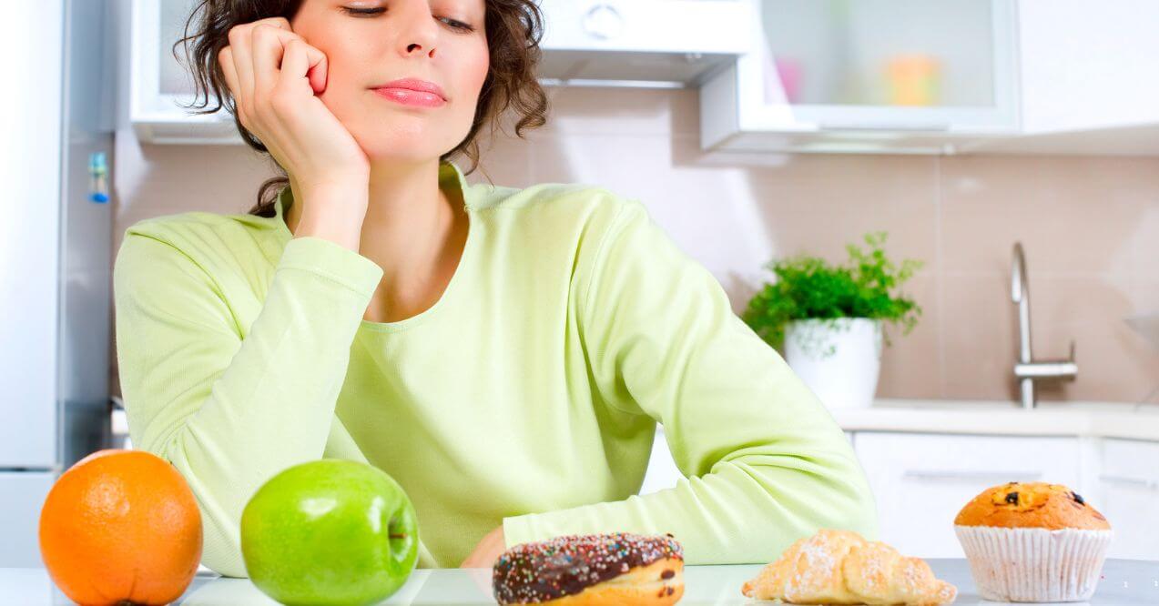 Woman deciding between healthy and unhealthy food options in a kitchen representing metabolic confusion.