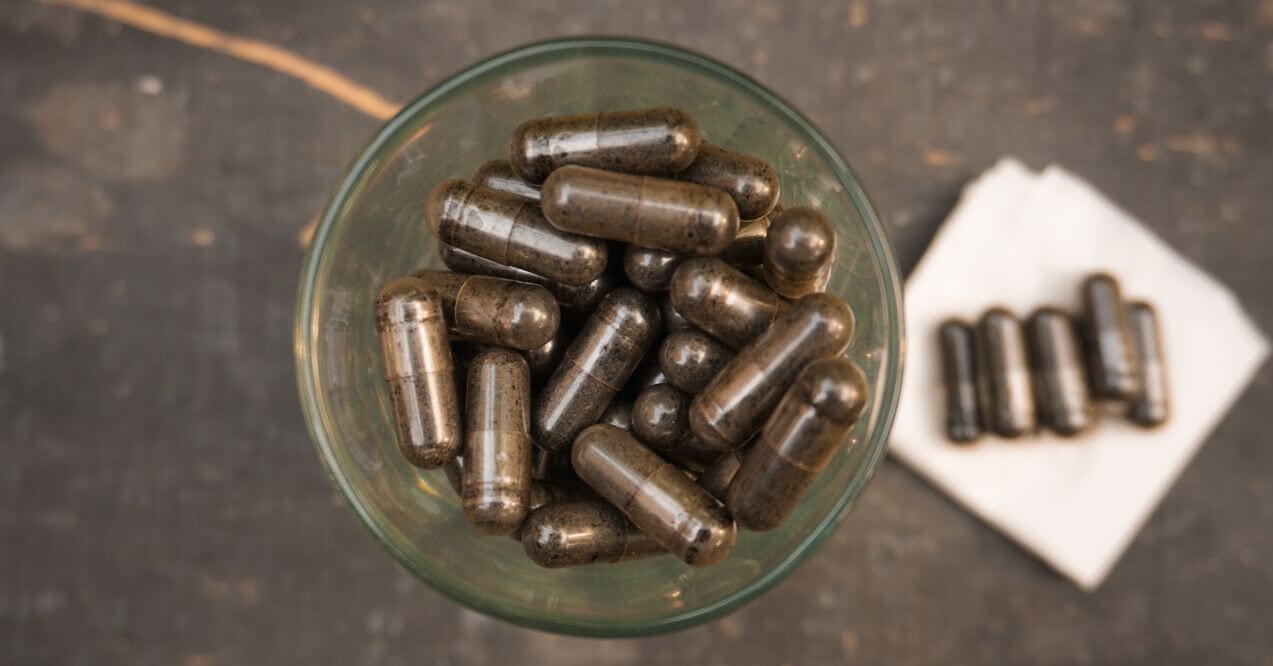 A glass filled with soil-based probiotics capsules on a dark surface.