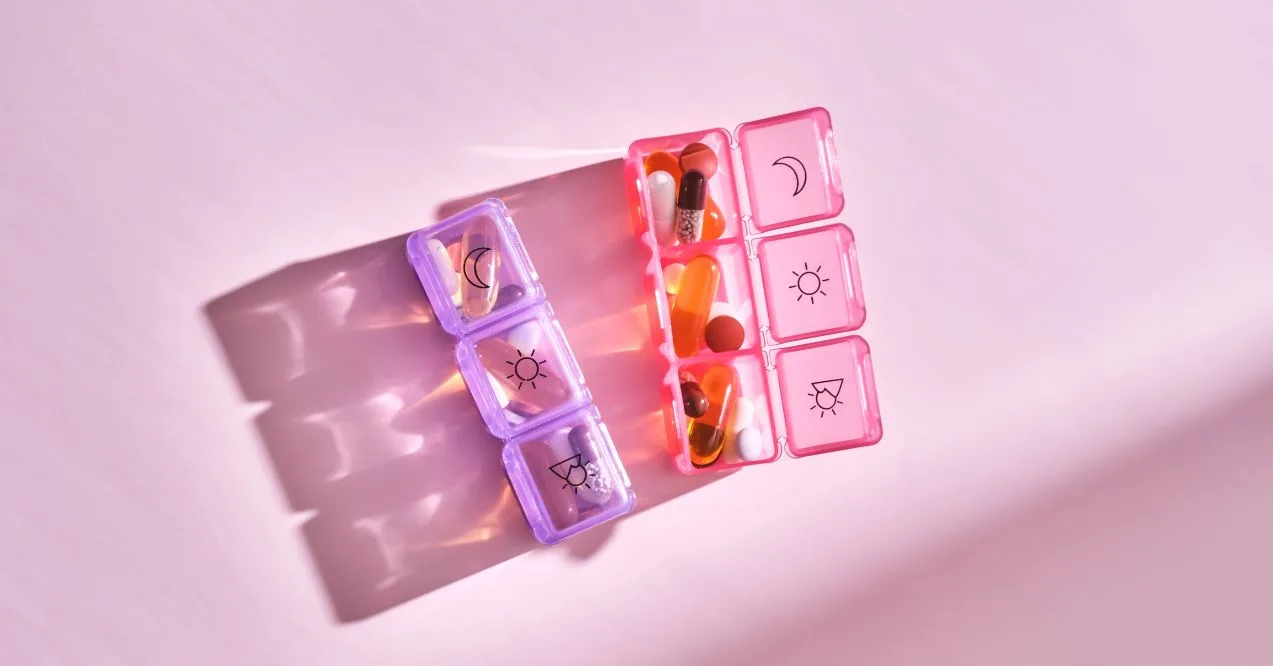 Pink and purple daily pill organizer filled with various supplements under soft lighting.