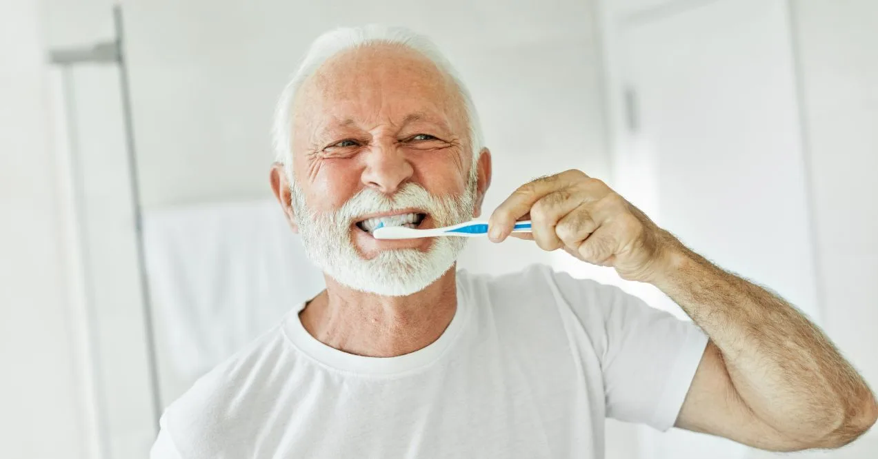 Elderly man smiling while brushing his teeth.