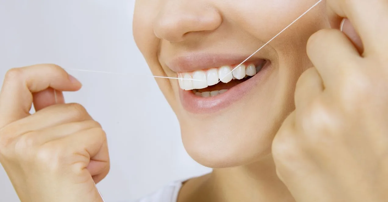 Woman flossing her teeth with a bright smile.