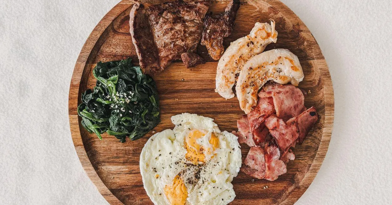 Wooden plate with protein-rich foods like eggs, steak, chicken, and greens.