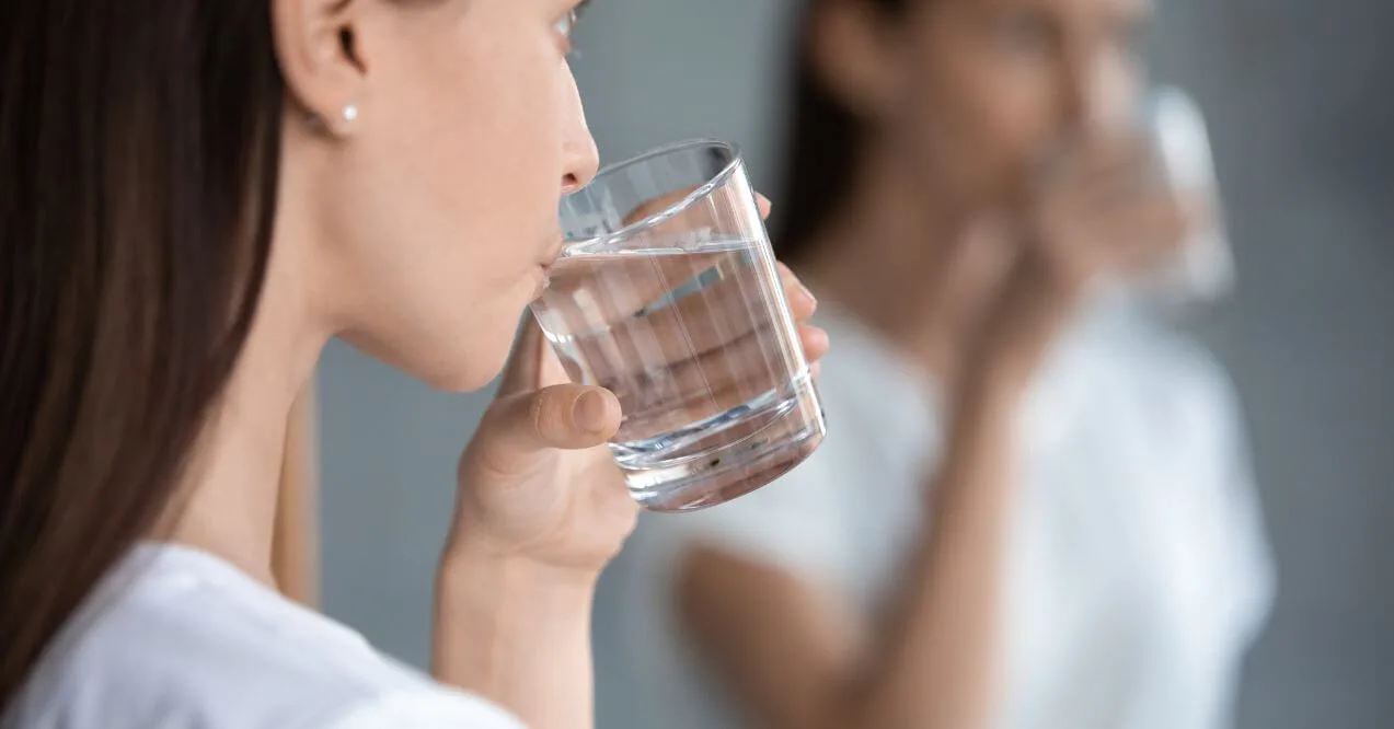 Close-up of a woman drinking a glass of water with a reflection in the mirror.