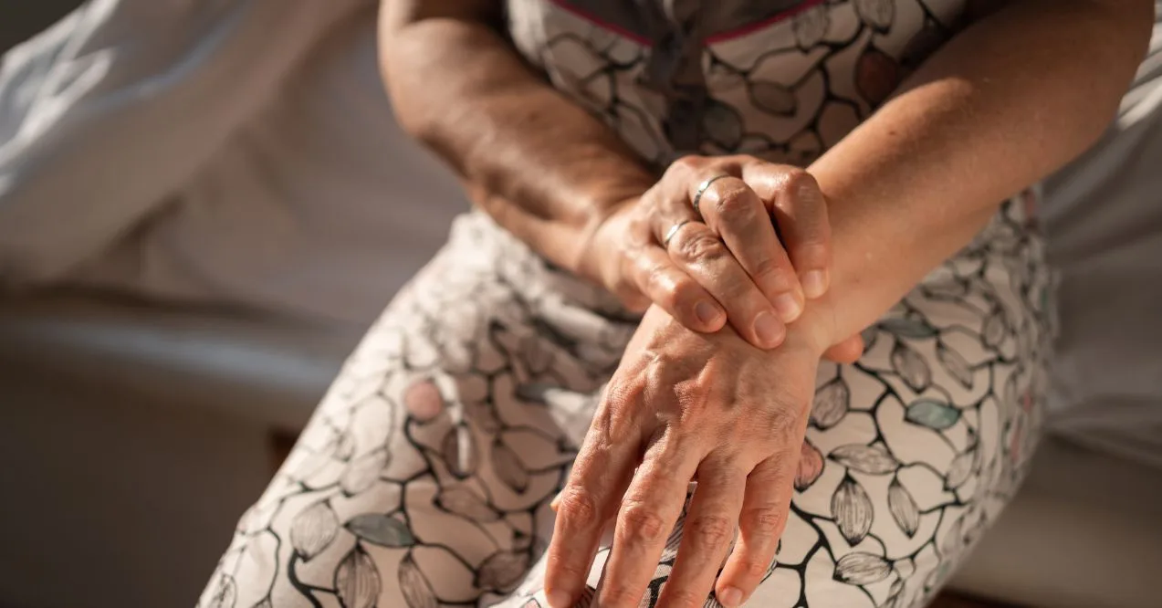 Older woman holding her wrist while sitting on a bed