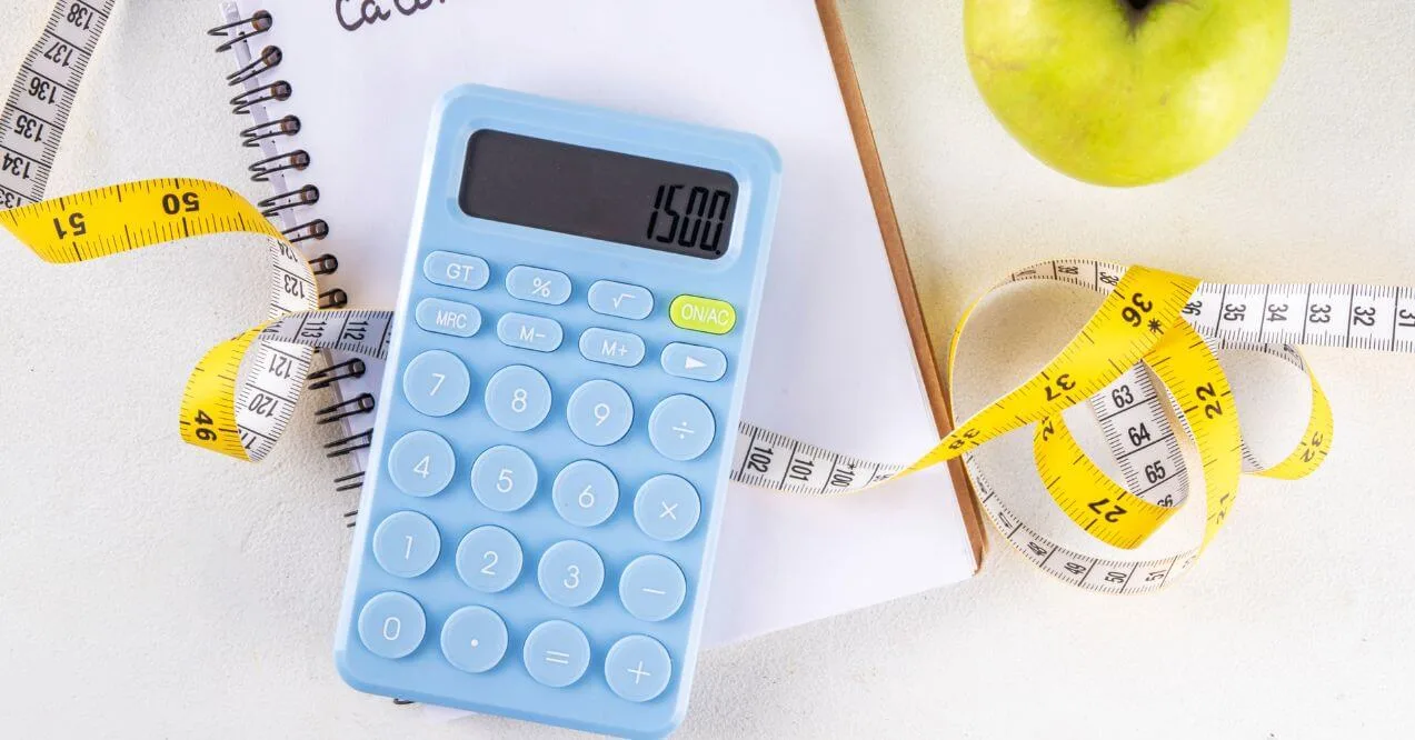 A blue calculator, measuring tape, apple, and notebook used for tracking calories.
