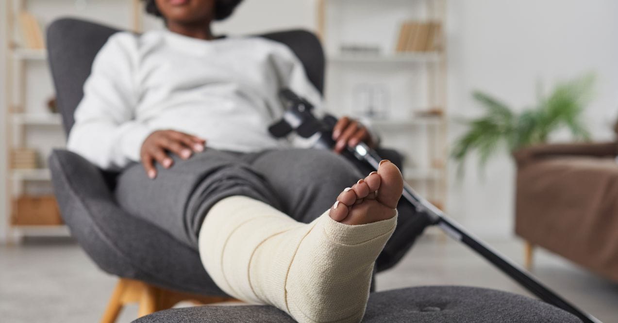 Person with a leg cast resting on a chair, indicating bone recovery wondering do broken bones heal stronger.