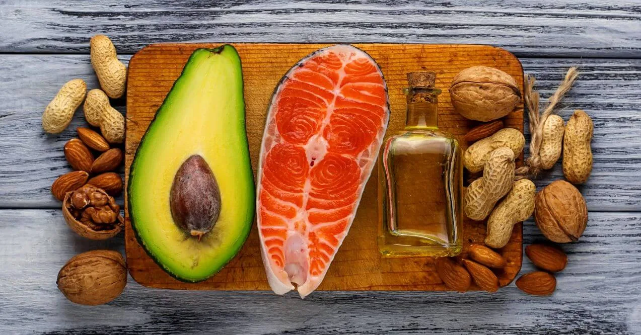 Avocado, salmon, nuts, and olive oil displayed on a wooden surface