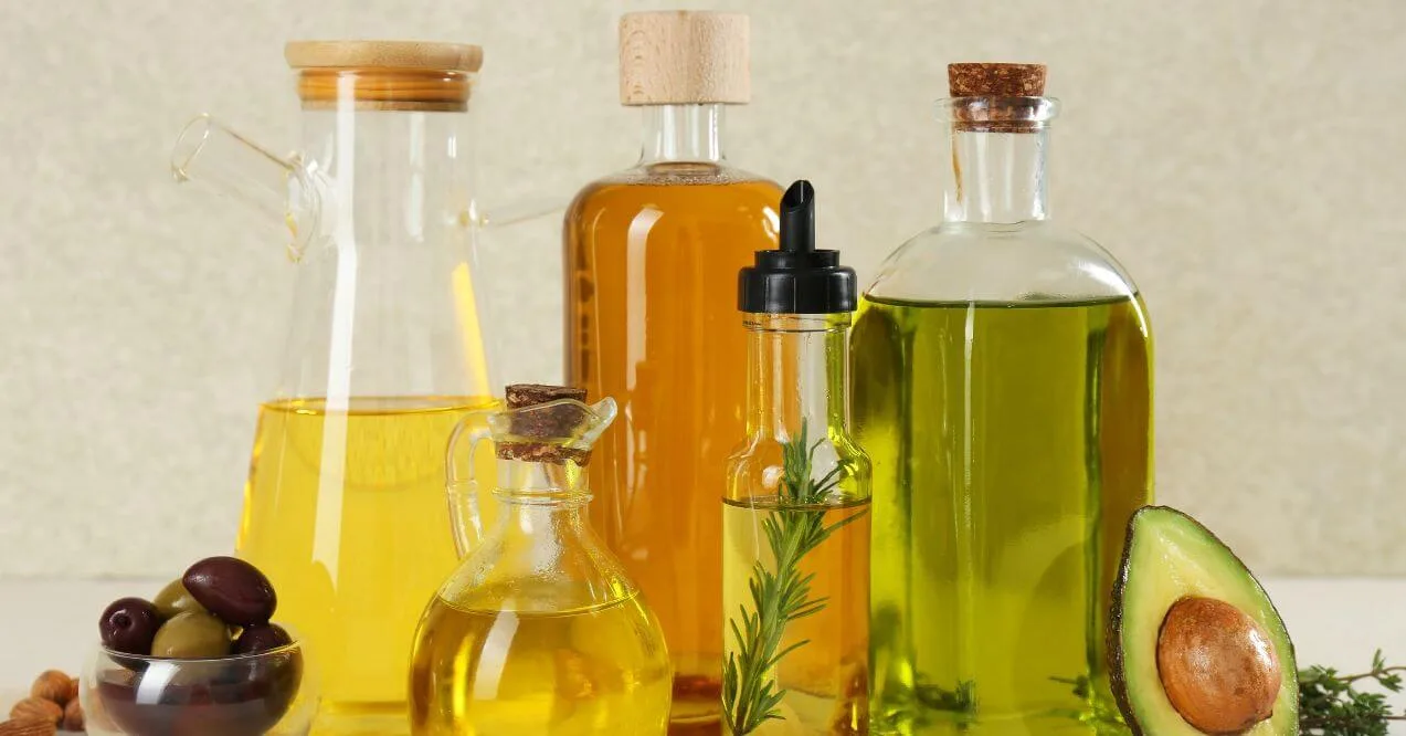 A variety of healthiest non-seed oils in glass bottles with herbs and olives.