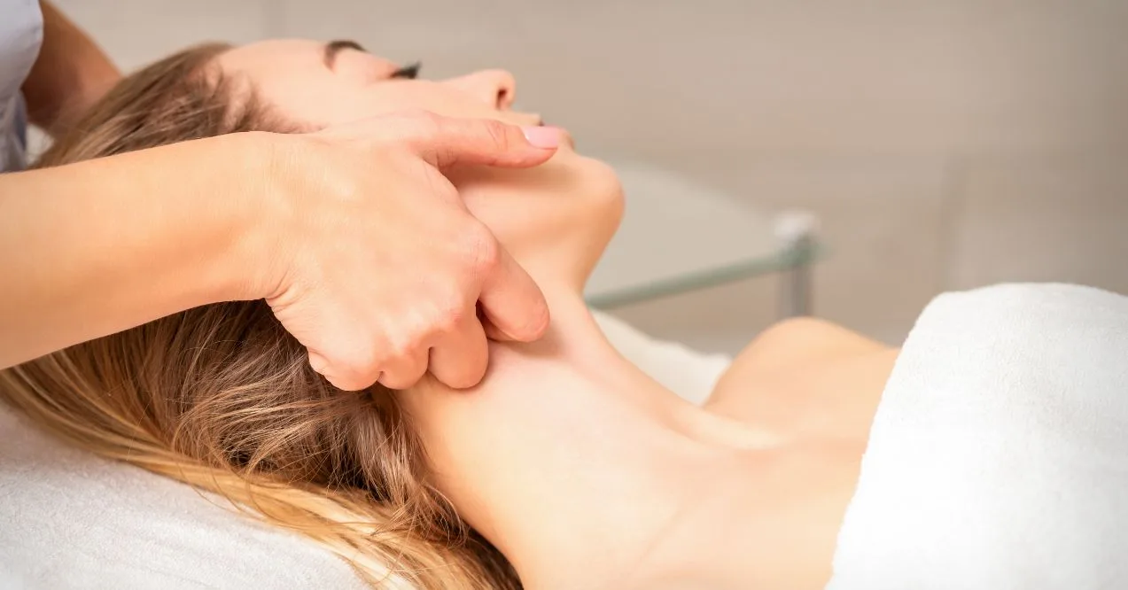 A therapist performing a gentle neck massage on a woman lying down in a spa setting.