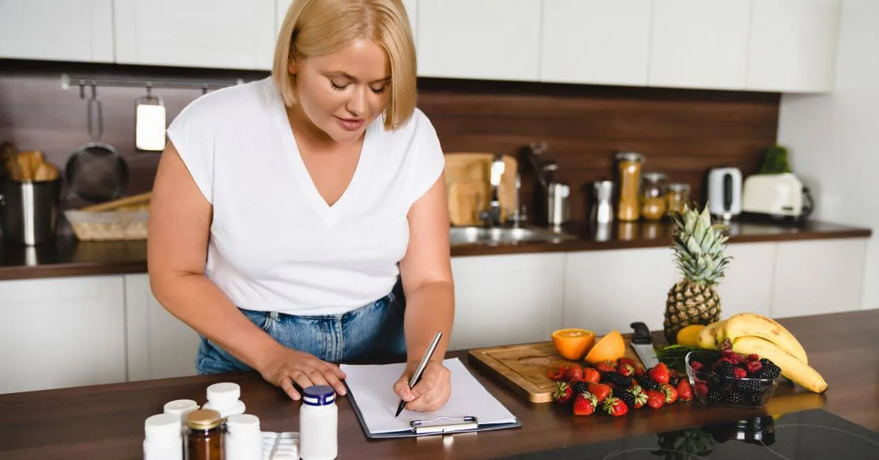 Woman writing in a notebook with fruits, supplements, and lymphedema diet items on a counter