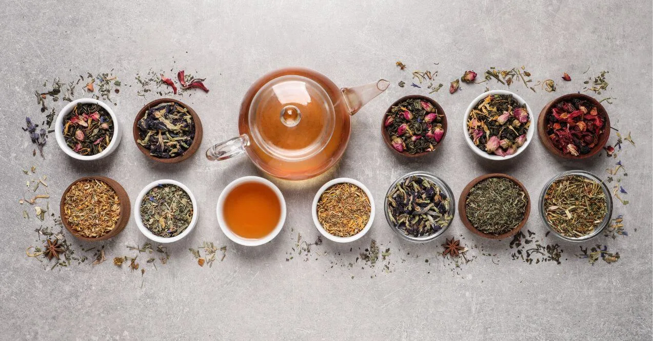 Glass teapot with herbal blends in small bowls, showcasing various types of tea for lymphatic system support.