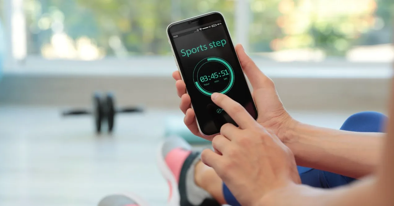 A person using a fitness tracking app on their phone while sitting in a workout space.