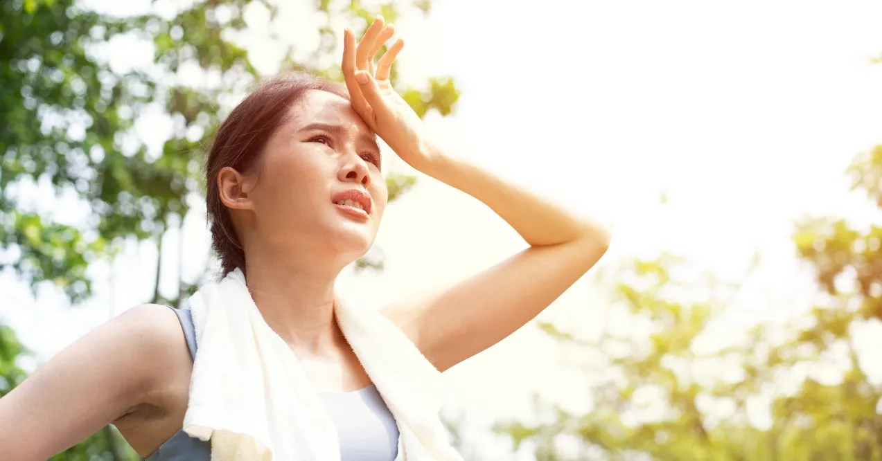 A sweaty woman outdoors wiping her forehead with her hand, wearing a towel around her neck wondering can dehydration cause swollen lymph nodes.