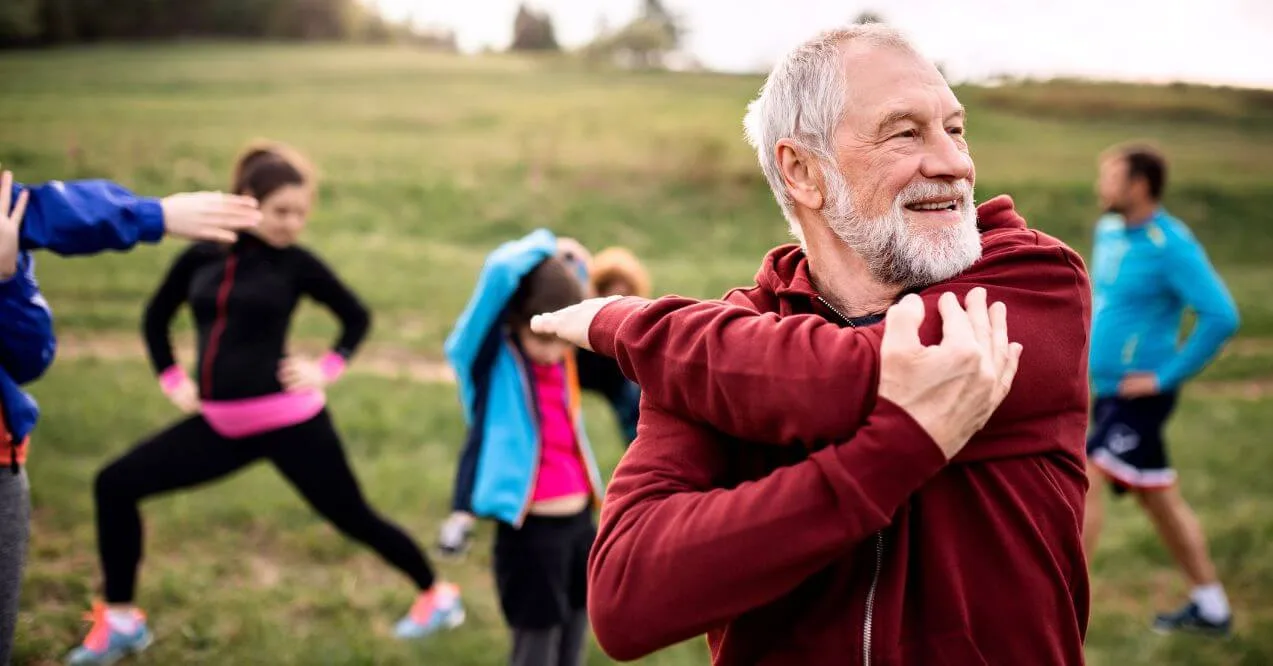 Group doing exercises for lymphatic drainage outdoors, with older man stretching in foreground
