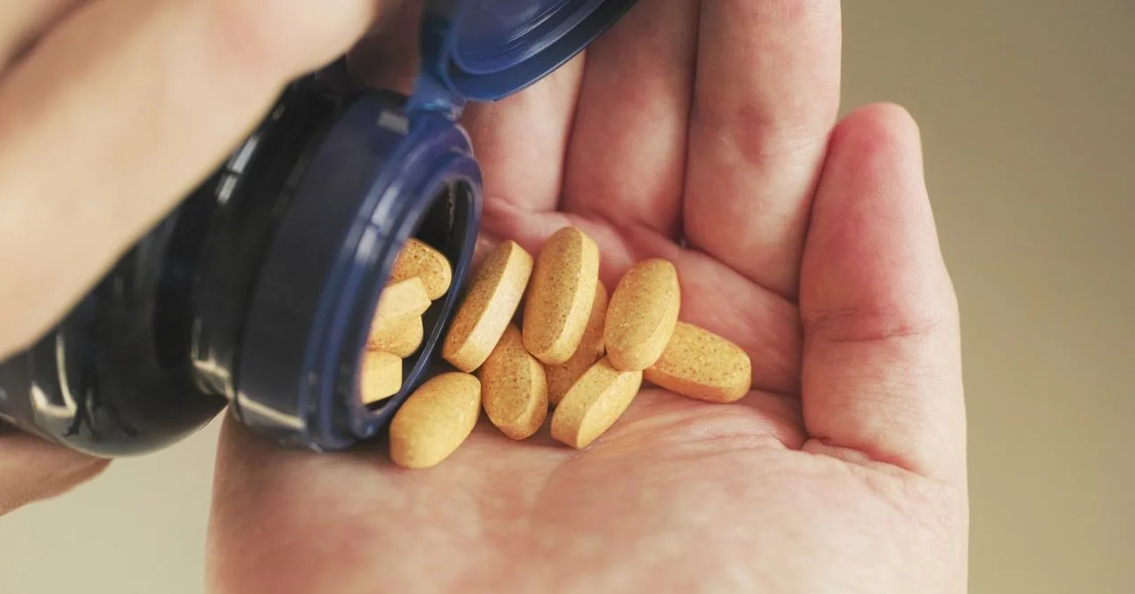 Close-up of a hand holding a bottle of vitamins, emphasizing fermented vitamins.