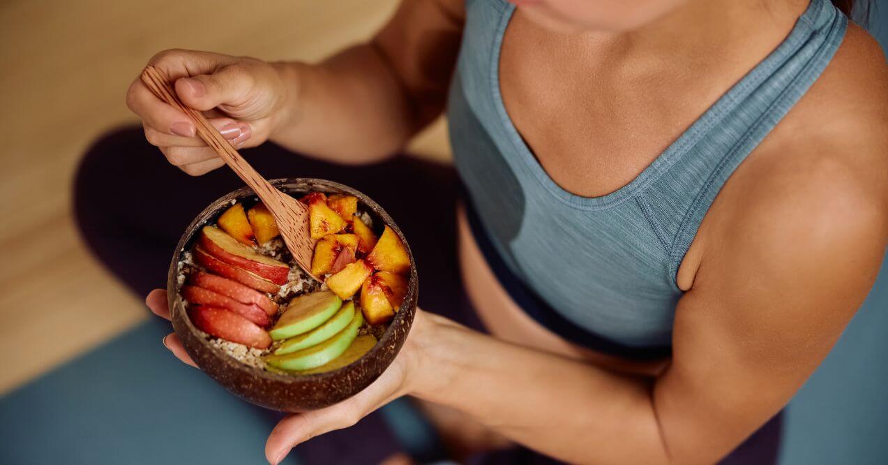Woman holding a bowl of oatmeal topped with sliced apples, peaches, and green fruit resembling foods good for lymphatic system.