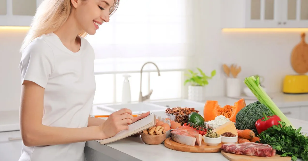 Woman writing meal plan at kitchen counter with keto-friendly fiber foods wondering how to get fiber on keto diet