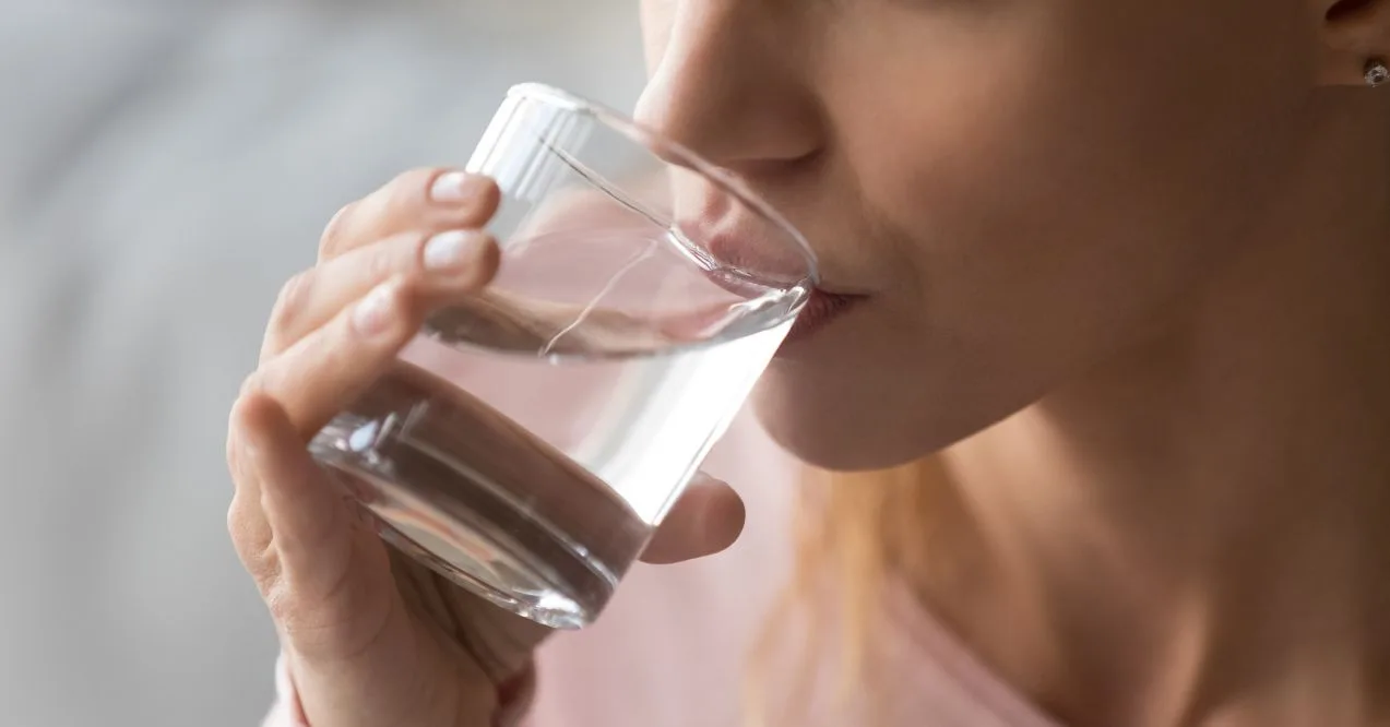 A close-up of a woman drinking a glass of water, focusing on her lips and the transparent glass.
