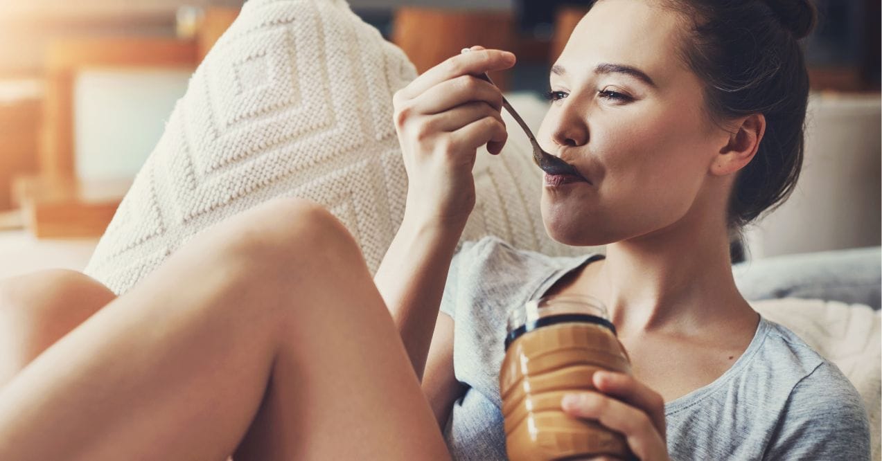 Smiling woman eating peanut butter with spoon on couch
