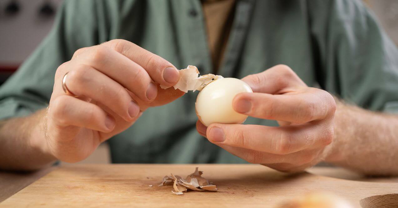 Person peeling a hard-boiled egg in kitchen resembling are eggs good for the lymphatic system.