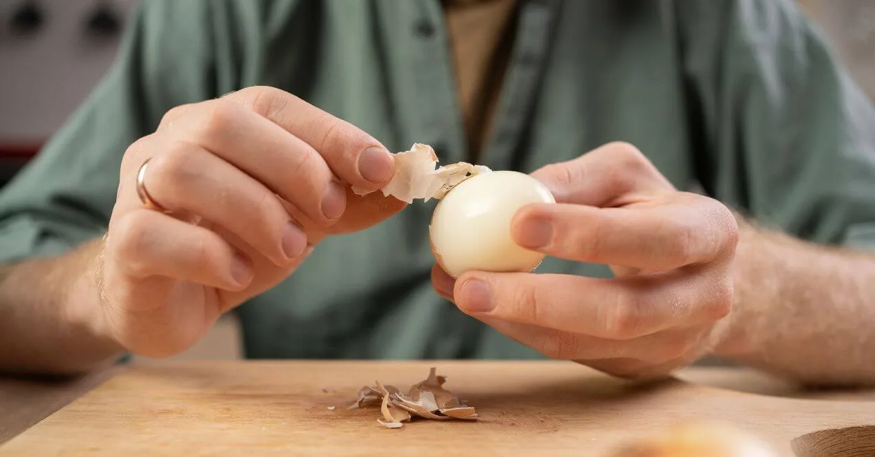 Person peeling a hard-boiled egg in kitchen resembling are eggs good for the lymphatic system.