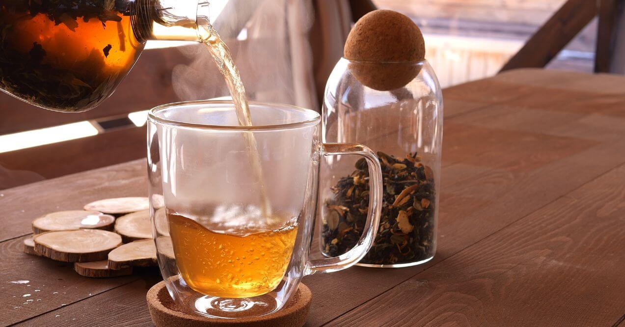 Pouring freshly brewed blue lotus tea into a glass cup.
