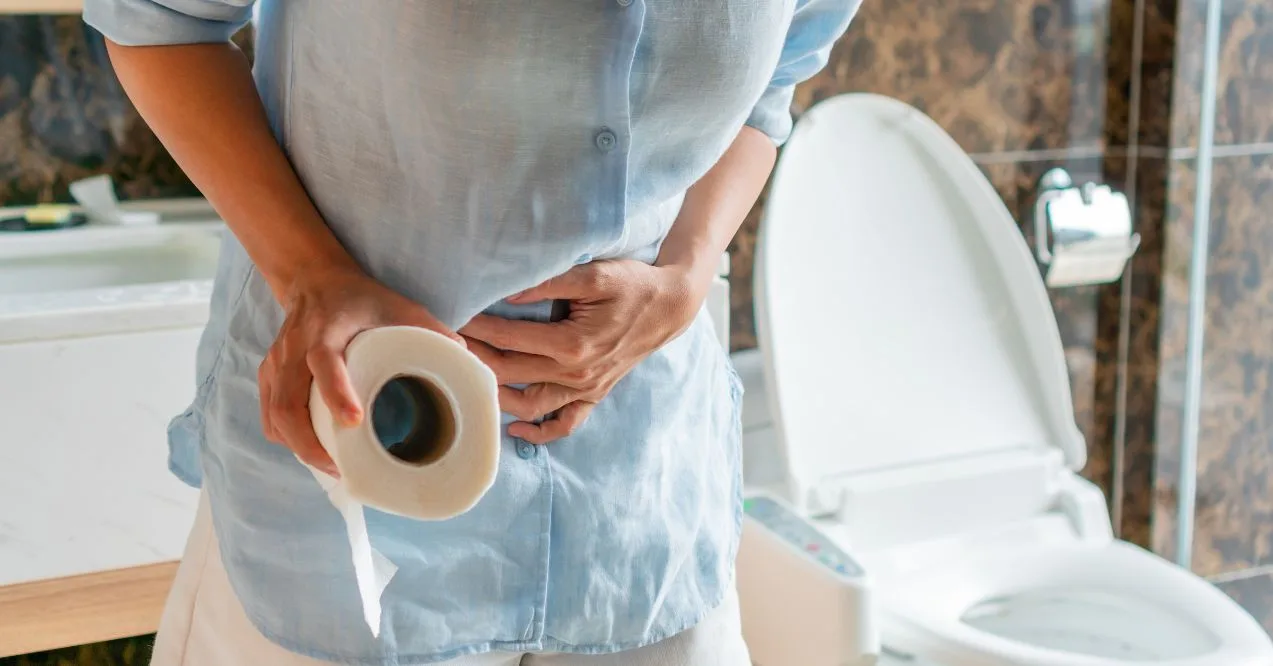 Person holding stomach and toilet paper near toilet, showing digestive discomfort from constipation and keto