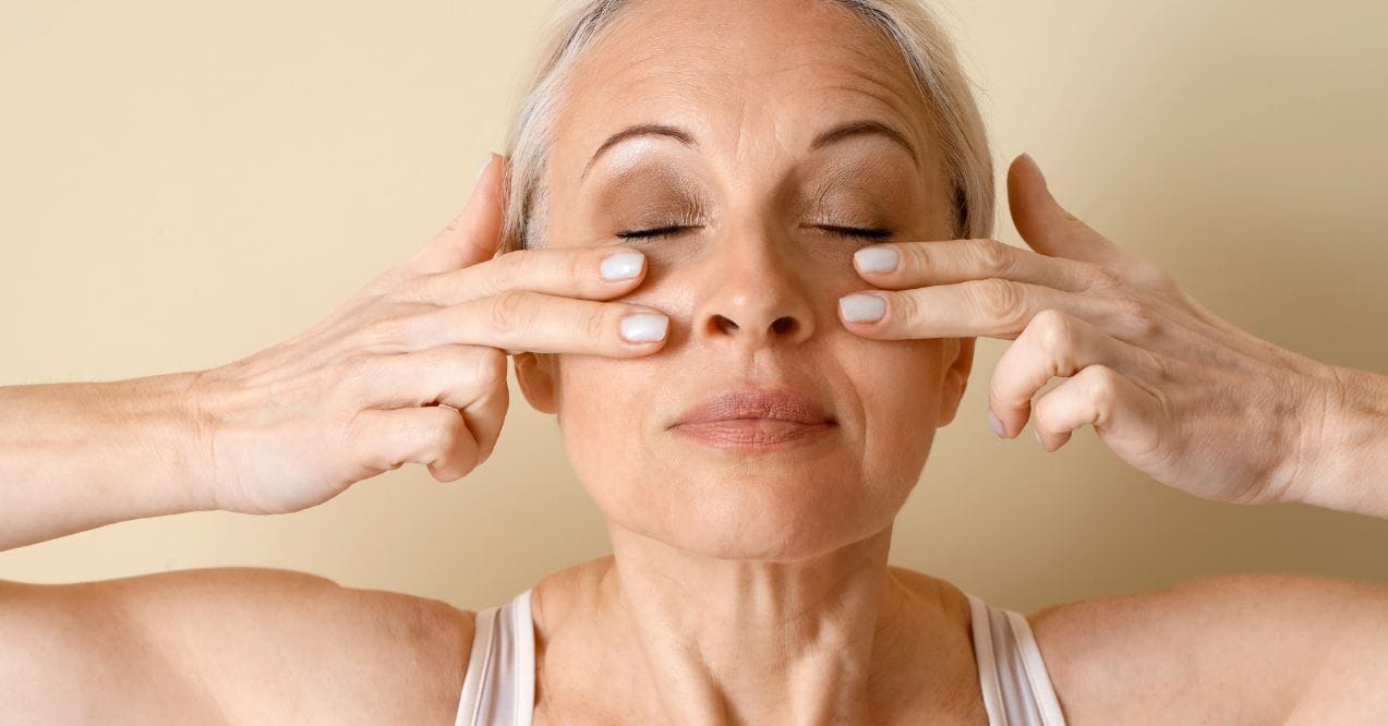 Woman using fingertips to gently massage area beneath her eyes resembling edema rehabilitation head and face exercises.