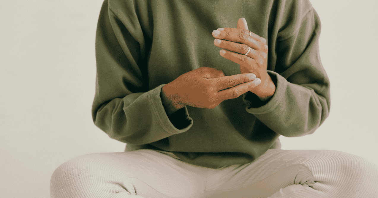 Zoomed in person sitting on the floor touching hands meditating