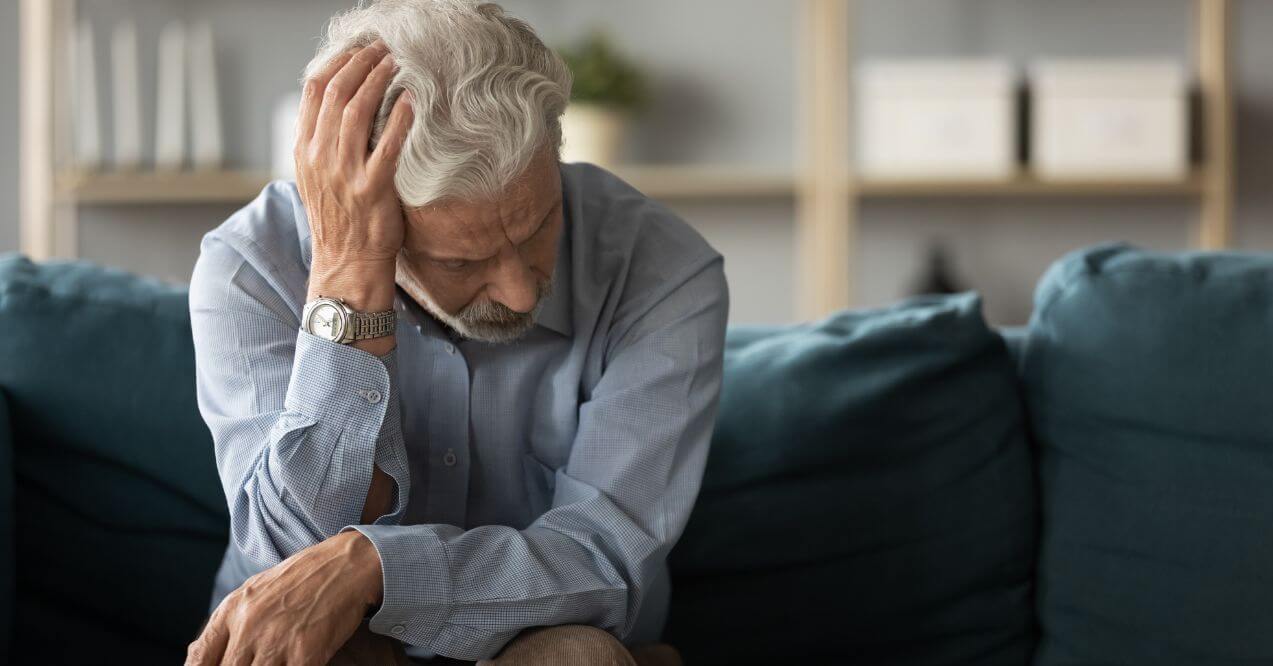 An elderly man sitting on a couch, showing signs of fatigue.
