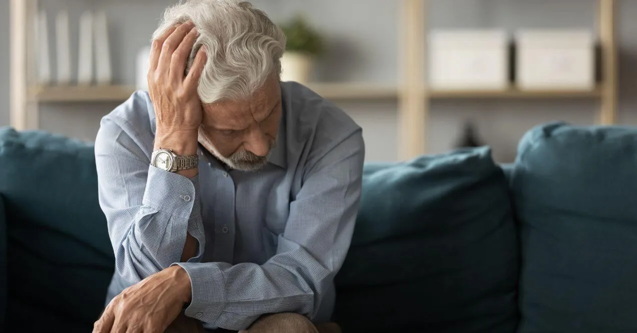 An elderly man sitting on a couch, showing signs of fatigue.