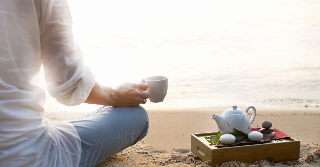 Person sipping tea in peaceful lakeside setting.