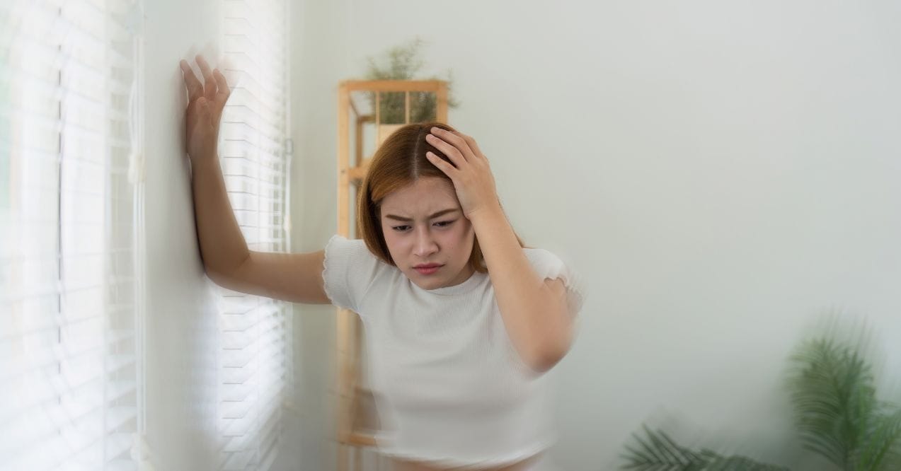Woman holding head and wall, experiencing dizziness, wondering can sinus cause dizziness.