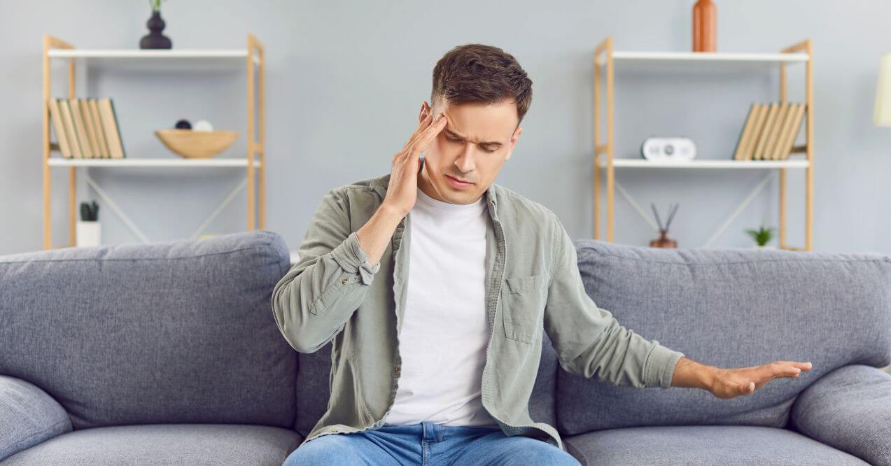 Man holding his head in pain, sitting on a couch, indicating does a pinched nerve cause headaches