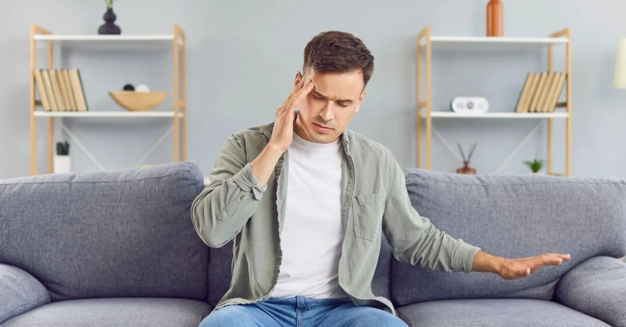 Man holding his head in pain, sitting on a couch, indicating does a pinched nerve cause headaches