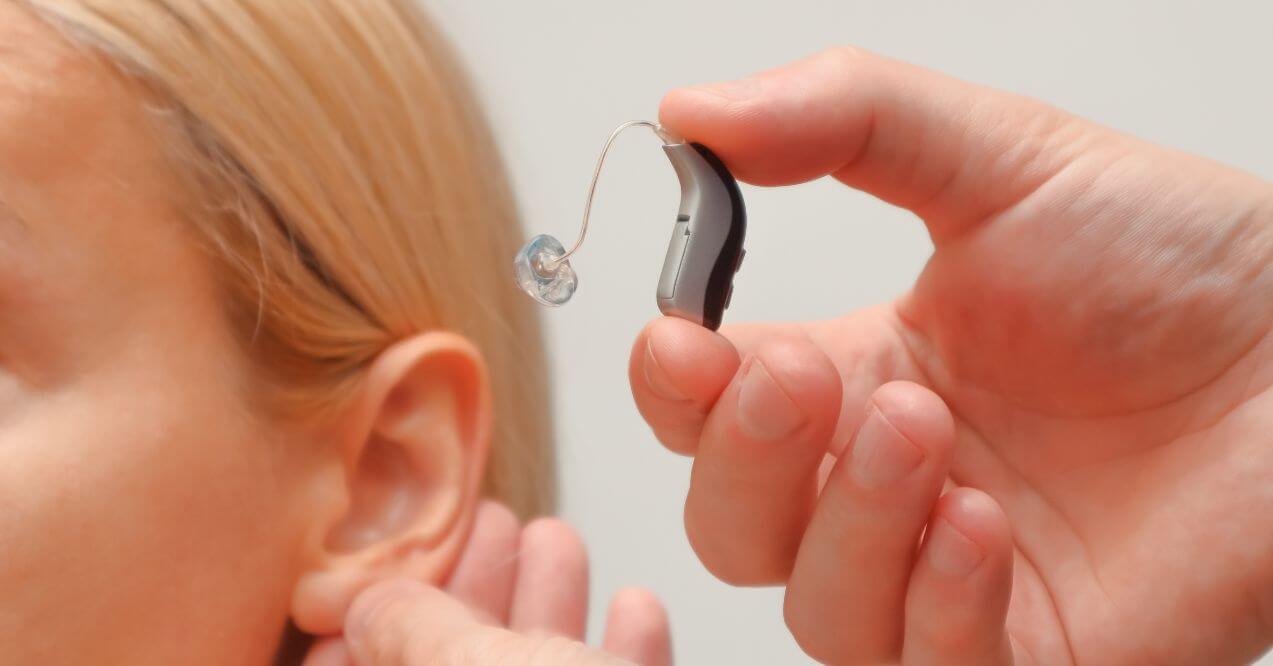 Close-up of a person adjusting a hearing aid showing negative side effects of hearing aids