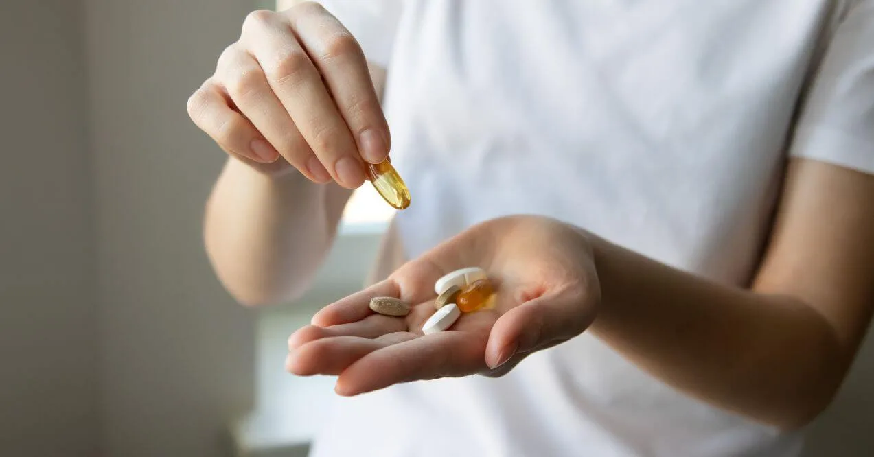 Hand holding various supplement pills resembling the topic can iron and vitamin d be taken together
