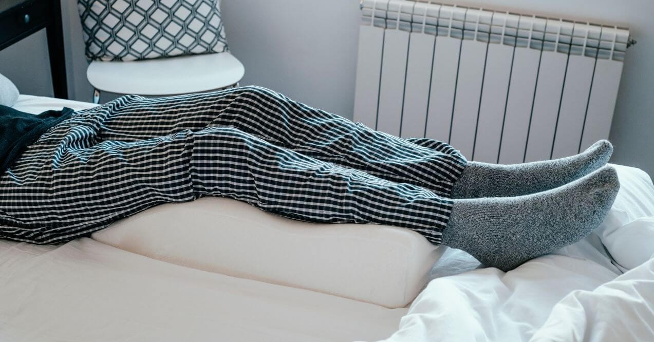 Person lying in bed with legs elevated on wedge cushion resembling is it good to sleep with your feet elevated