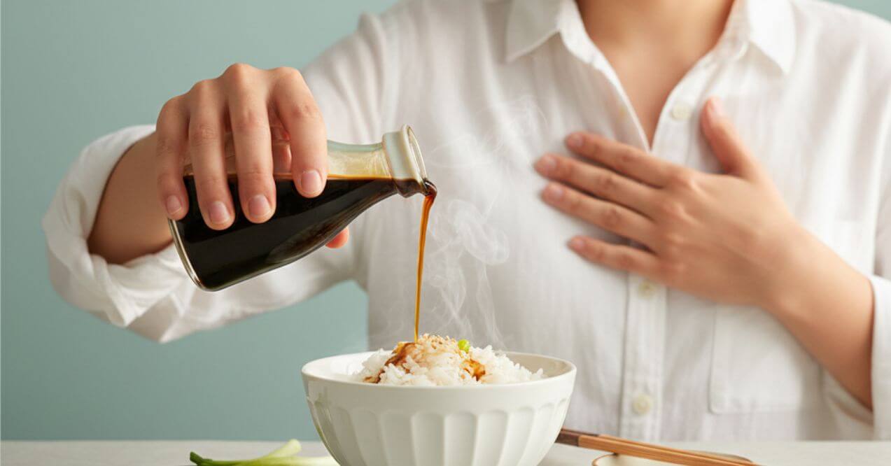 Person holding chest while pouring soy sauce on rice wondering does soy sauce cause heartburn.